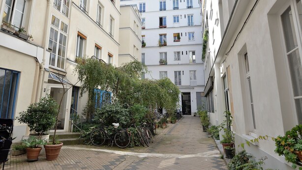 A narrow alleyway with buildings on either side, potted plants, and bicycles. - Appartement Charenton - Welkeys (Paris)