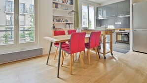 A modern kitchen with a dining area, large windows, and a bookshelf. - Appartement Charenton - Welkeys (Paris)