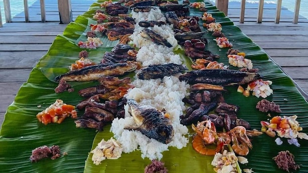 A long table with a variety of dishes, including fish and rice, set up on a wooden deck overlooking the ocean. - Pamana Beach House  (Calatagan)