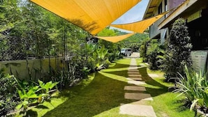 A pathway leading to a building with a covered area, surrounded by greenery and a clear sky. - Pamana Beach House  (Calatagan)