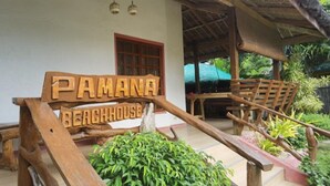 A wooden sign reading "PAMANA BEACHHOUSE" with a rustic design, wooden benches, and a thatched roof structure. - Pamana Beach House  (Calatagan)