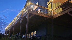 Un edificio de dos pisos con una terraza y barandilla de madera, rodeado de vegetación.