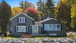 A two-story house with a stone foundation, large windows, and a front porch with a bench. - Sunshine Cove - Door County (Sturgeon Bay)