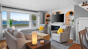A living room with a sofa, armchairs, a fireplace, a TV, and a view of the sea. - Sunshine Cove - Door County (Sturgeon Bay)