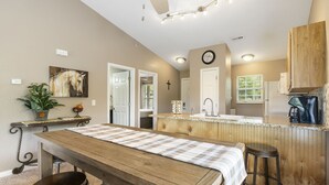 A kitchen with a wooden table, bar stools, a sink, and a clock on the wall.