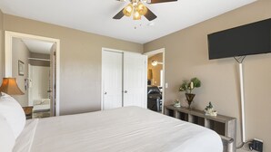 A hotel room with a large bed, a ceiling fan, a flat-screen TV, and a bedside table with a lamp.