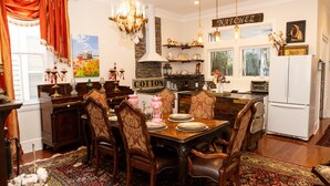 A dining area with a wooden table set for six, surrounded by ornate chairs. A chandelier hangs above, and a sign reading "NATCHEZ" is visible on the wall. - The Dollhouse | 3/2 | Walk to Downtown (Natchez)