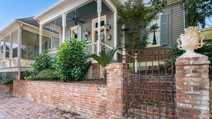 A traditional house with a covered porch, brick wall, and decorative iron gate. - The Dollhouse | 3/2 | Walk to Downtown (Natchez)