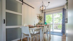 Un comedor con una mesa preparada para cuatro, sillas blancas, una araña y vistas al exterior a través de una puerta corrediza de vidrio.