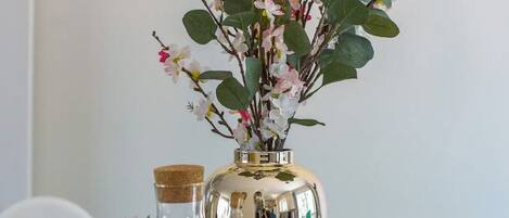 Een gedekte tafel met glazen flessen, een metalen vaas met roze bloemen en een glas water.