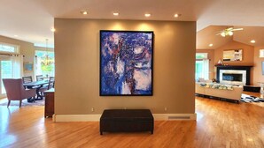 Un salón amplio con un cuadro abstracto grande en la pared, una chimenea y un comedor visible a través de una puerta abierta.
