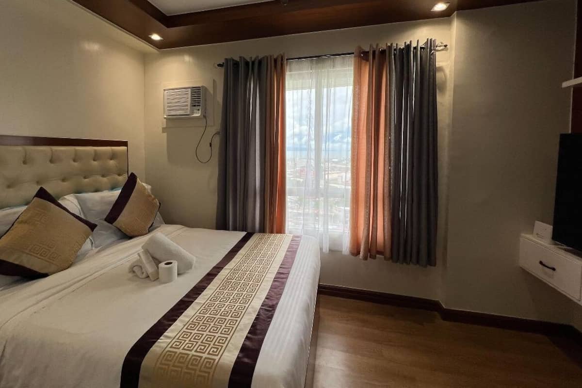 Une chambre d’hôtel avec un grand lit, une télévision et une fenêtre avec des rideaux.