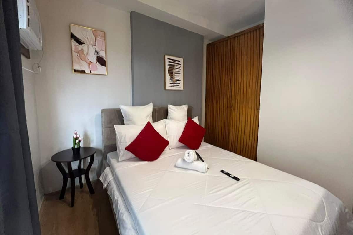 Une chambre d’hôtel bien rangée, avec un lit, une petite table ronde ornée d’un vase de fleurs et deux tableaux accrochés au mur.