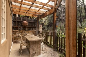 A covered patio with a stone wall, wooden table, and chairs.