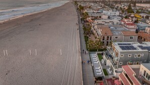 Een hotel aan de kust met een uitgestrekt strand, meerdere gebouwen en een rij ligbedden langs de zijkant.