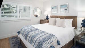 Een slaapkamer met een bed, een plafondventilator, een nachtkastje, een lamp, een spiegel en twee ingelijste foto's aan de muur.