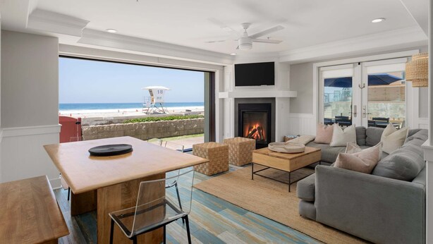 A living room with a fireplace, a sofa, a coffee table, and a view of the beach. - Oceanfront | Private Ground Floor Patio | Hot Tub (San Diego)