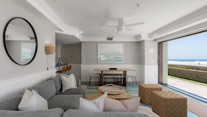A modern living room with a gray sofa, a wooden coffee table, and a view of the beach through a large window. - Oceanfront | Private Ground Floor Patio | Hot Tub (San Diego)