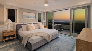 A bedroom with a bed, nightstands, a ceiling fan, a large window with a view of the beach, and a sliding glass door leading to an outdoor area. - Oceanfront | Private Ground Floor Patio | Hot Tub (San Diego)