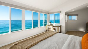Une chambre dotée d’un grand lit, d’un bureau et offrant une vue sur l’océan grâce à de nombreuses fenêtres.