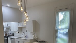 A modern kitchen with a central island, bar stools, pendant lighting, and a view of the outdoors through a window. - Private Vacation Home with large Hot Tub and Fire Pit -- Sleeps 18 (Gibsonia)