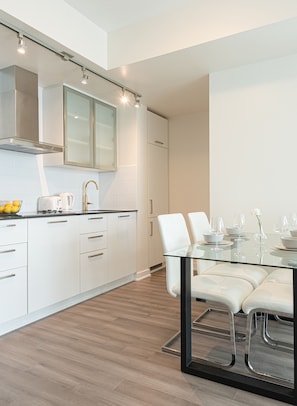 A modern kitchen with white cabinetry, a glass dining table, and a stainless steel range hood. - Beautiful Luxurious Modern With Breathtaking Views  (Toronto)