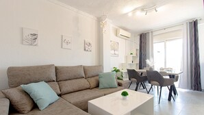 A modern living room with a beige sofa, a white coffee table, and a dining area with a table and chairs. - Beach front apartment in Torrevieja with WiFi (Torrevieja)