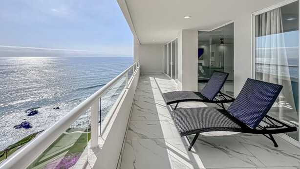 Un balcon avec deux chaises et une porte vitrée donnant sur une pièce. Le balcon offre une vue sur une étendue d’eau.