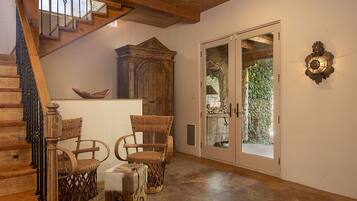 Una escalera de madera con una puerta de vidrio que da al exterior. Hay sillones de mimbre y un mueble de madera en la habitación.