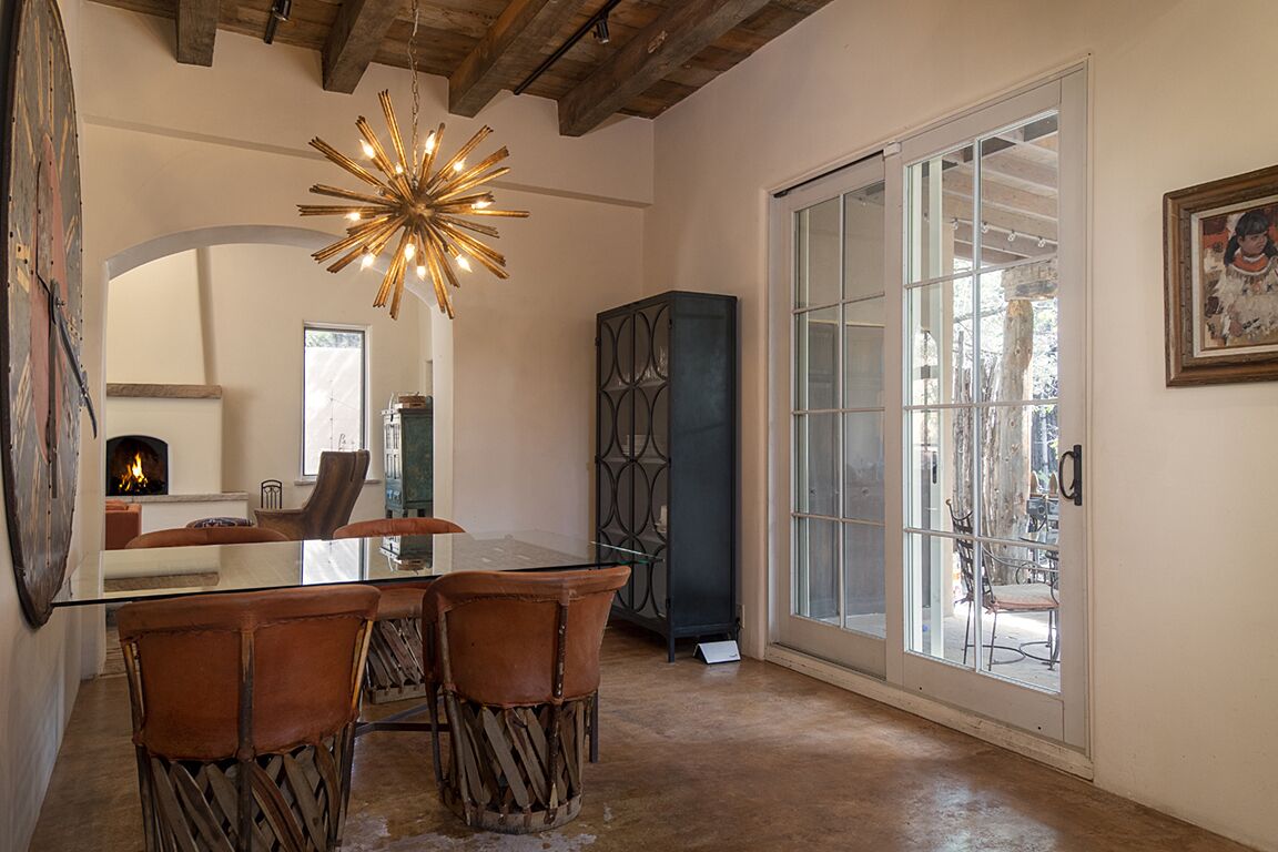 A dining area with a glass table, leather chairs, a starburst chandelier, and a view through a glass door.