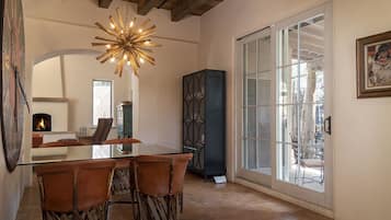 A dining area with a glass table, leather chairs, a starburst chandelier, and a view through a glass door.