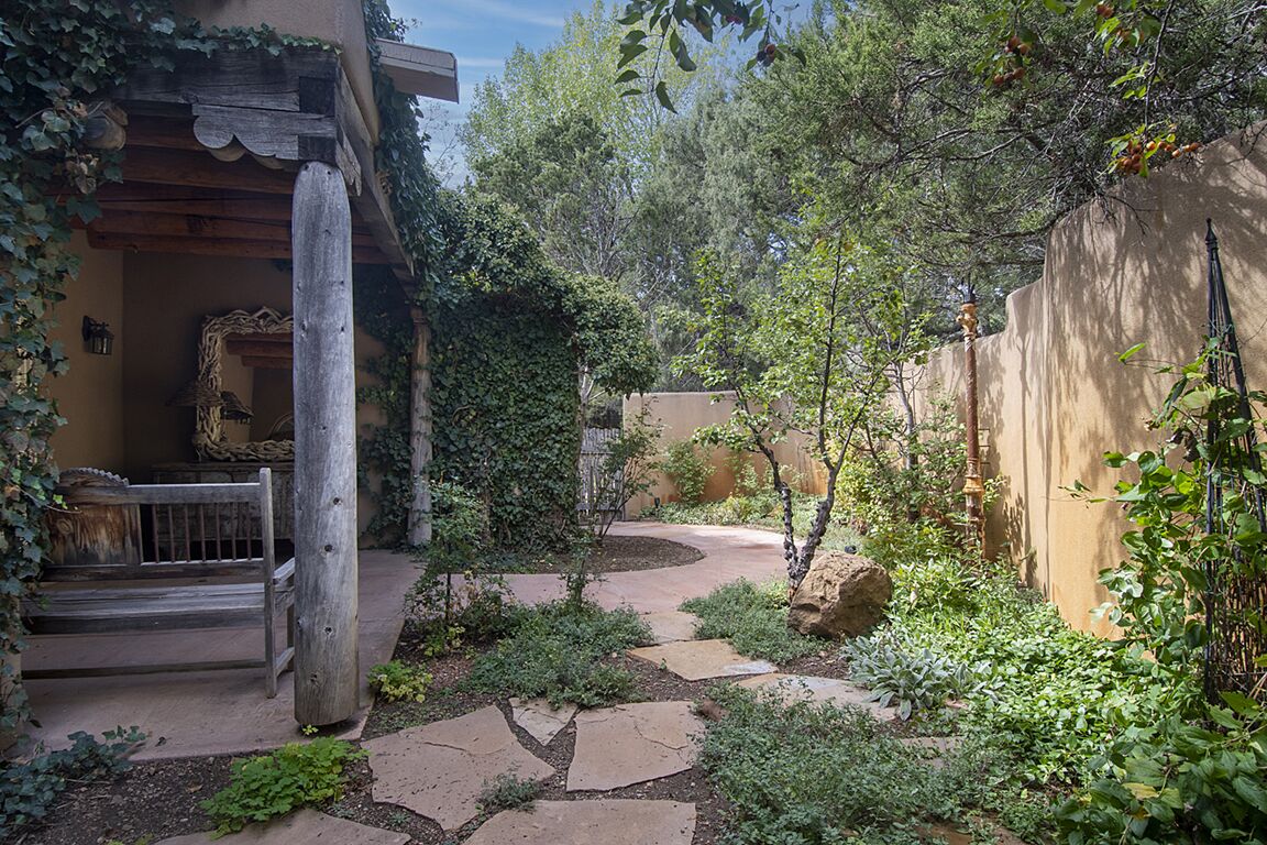 Un patio con sendero de piedra, pérgola de madera y abundante vegetación.