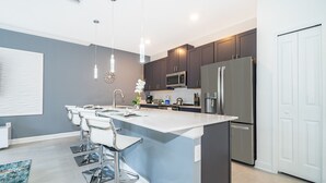Une cuisine moderne dotée d’un îlot central, de meubles de couleur sombre, d’appareils électroménagers en acier inoxydable et d’une porte blanche.