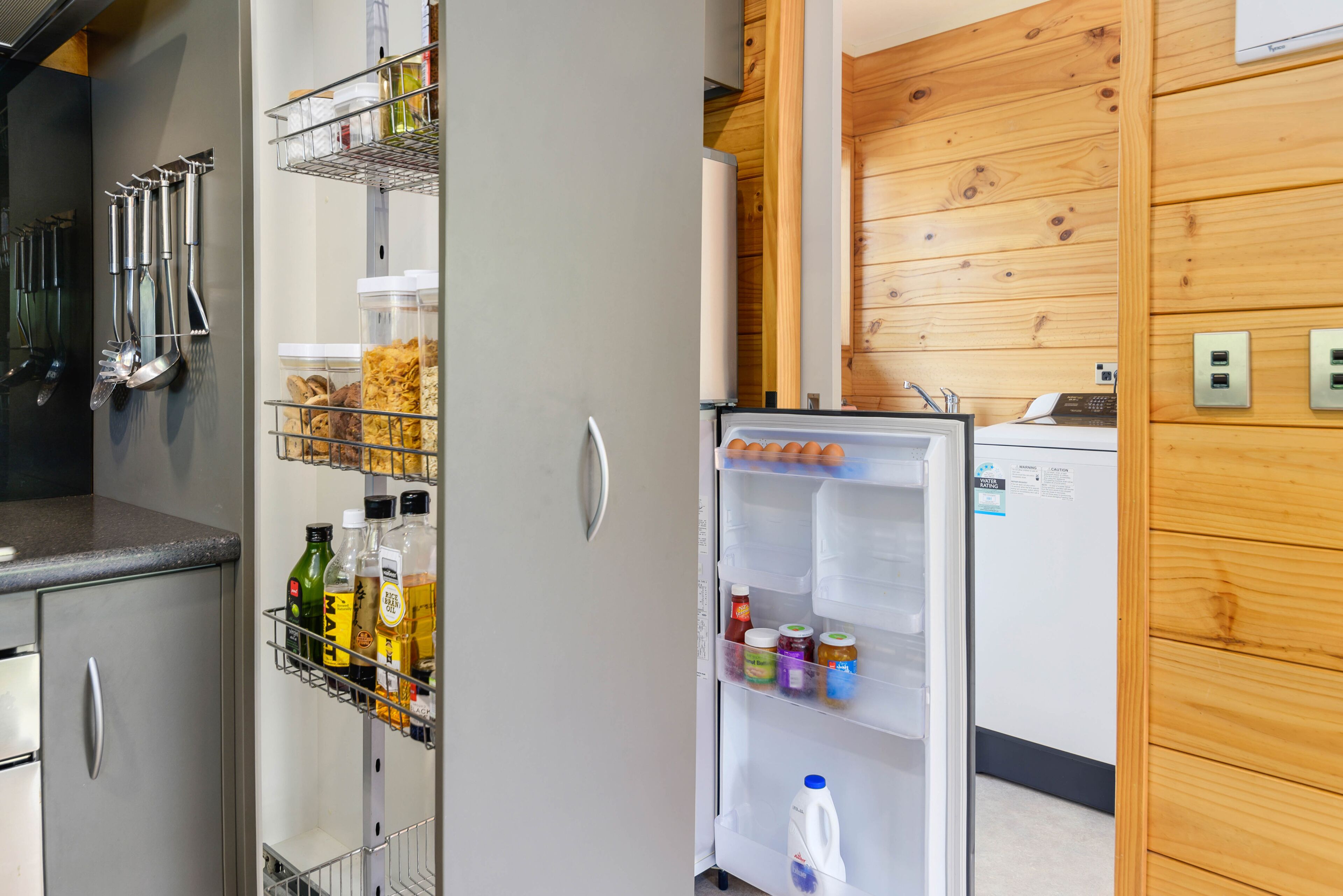A kitchen with a refrigerator, a metal rack with bottles, and a wooden wall.