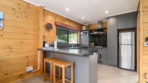 Una cucina moderna con rivestimenti in legno, un'isola centrale con sgabelli, elettrodomestici in acciaio inossidabile e un'ampia finestra.