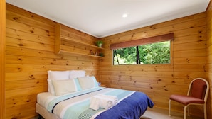 Una stanza con rivestimenti in legno, un letto, una sedia e una finestra vista alberi.
