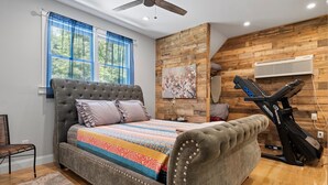Une chambre avec un lit à capitonnage, un ventilateur de plafond, un tapis de course et un mur en bois.