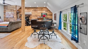 Un vaste espace de vie agrémenté d’un mur en bois, d’une table à manger ronde et d’une grande fenêtre avec des rideaux.