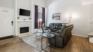 A living room with a fireplace, a sofa, a coffee table, and a TV mounted on the wall. - 5 STAR Townhome near all major highways! Fast Wifi (Carrollton)