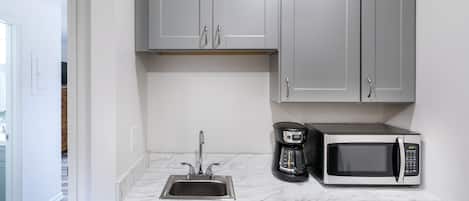 Una cocina compacta con un lavamanos, cafetera y microondas.