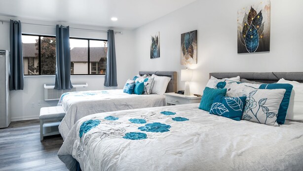 Une chambre d’h ôtel avec deux lits, une fenêtre avec des rideaux, une table de chevet avec une lampe et des œuvres d’art accrochées au mur.