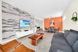 Ein modernes Wohnzimmer mit Couch in Grau, einem Holztisch und einer orangefarbenen Wand.