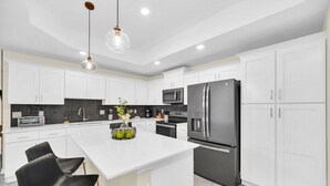 A modern kitchen with white cabinets, a black refrigerator, a microwave, and a large island with two black chairs.