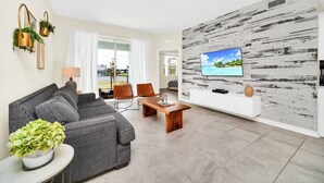 A modern living room with a grey sofa, wooden coffee table, and a TV mounted on a white wall with a distressed wood panel design.