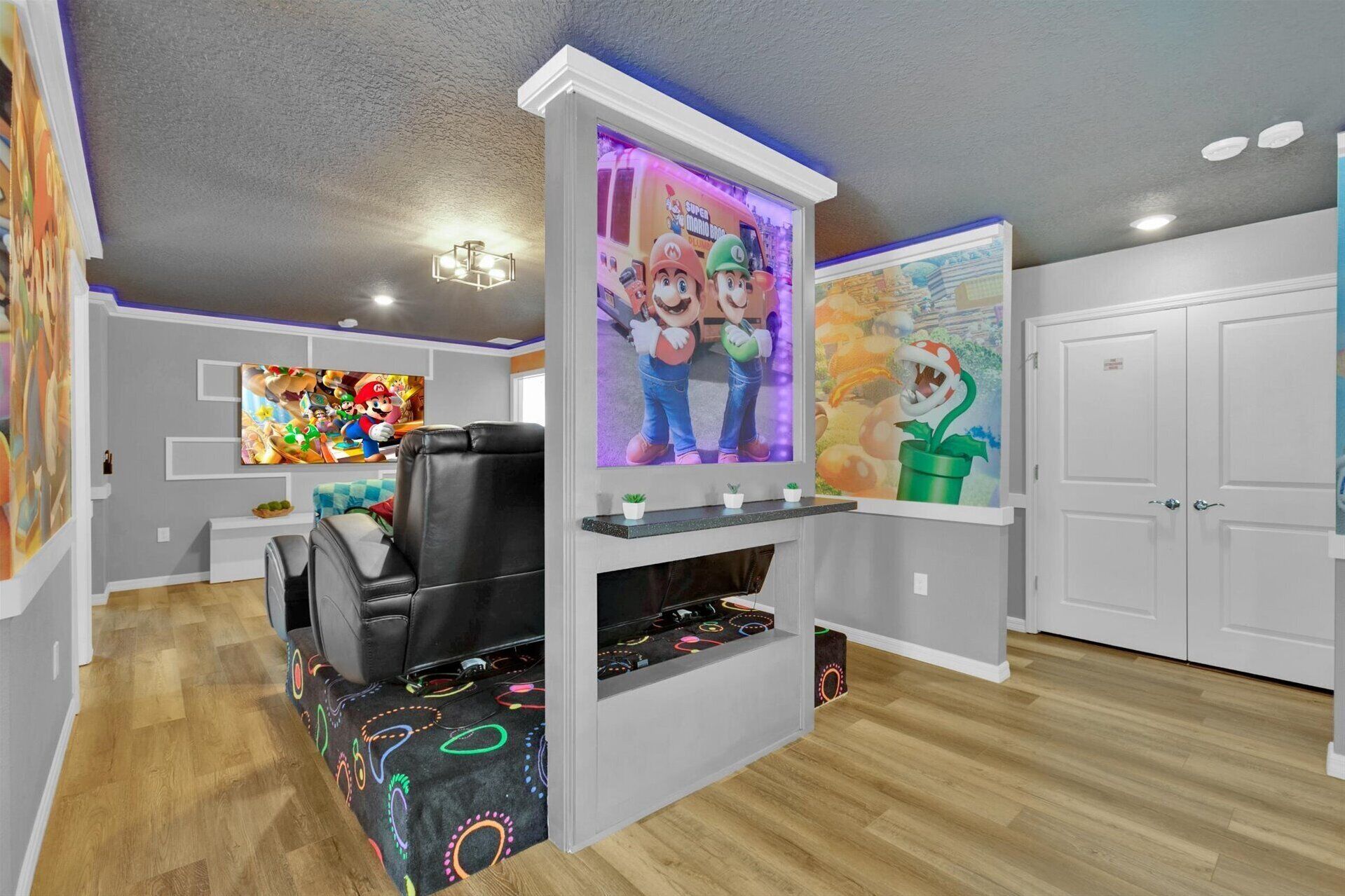 A living room with a black leather sofa, a flat-screen TV, and a wall-mounted gaming console.
