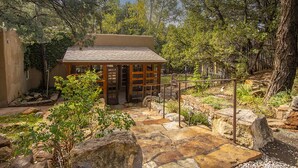A rustic cabin with a stone patio, surrounded by trees and a stone wall. - Tranquil compound directly across from 10,000 waves and close to town and skiing (Santa Fe)