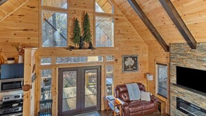 A spacious cabin with a loft bedroom, a cozy living area with a leather sofa, and a stone fireplace. - EagleRock Retreat | Pet Friendly w/ Hot Tub, Firepit + WiFi (Rogers)