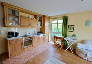 Cozinha compacta com armários de madeira, forno embutido e um espaço de refeições com mesa e cadeira.