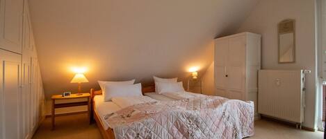 A bedroom with a large bed, two bedside tables with lamps, a wardrobe, and a radiator.