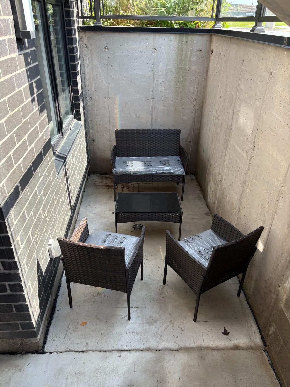 A small outdoor patio area with a table and two chairs, enclosed by a brick wall and a concrete floor.